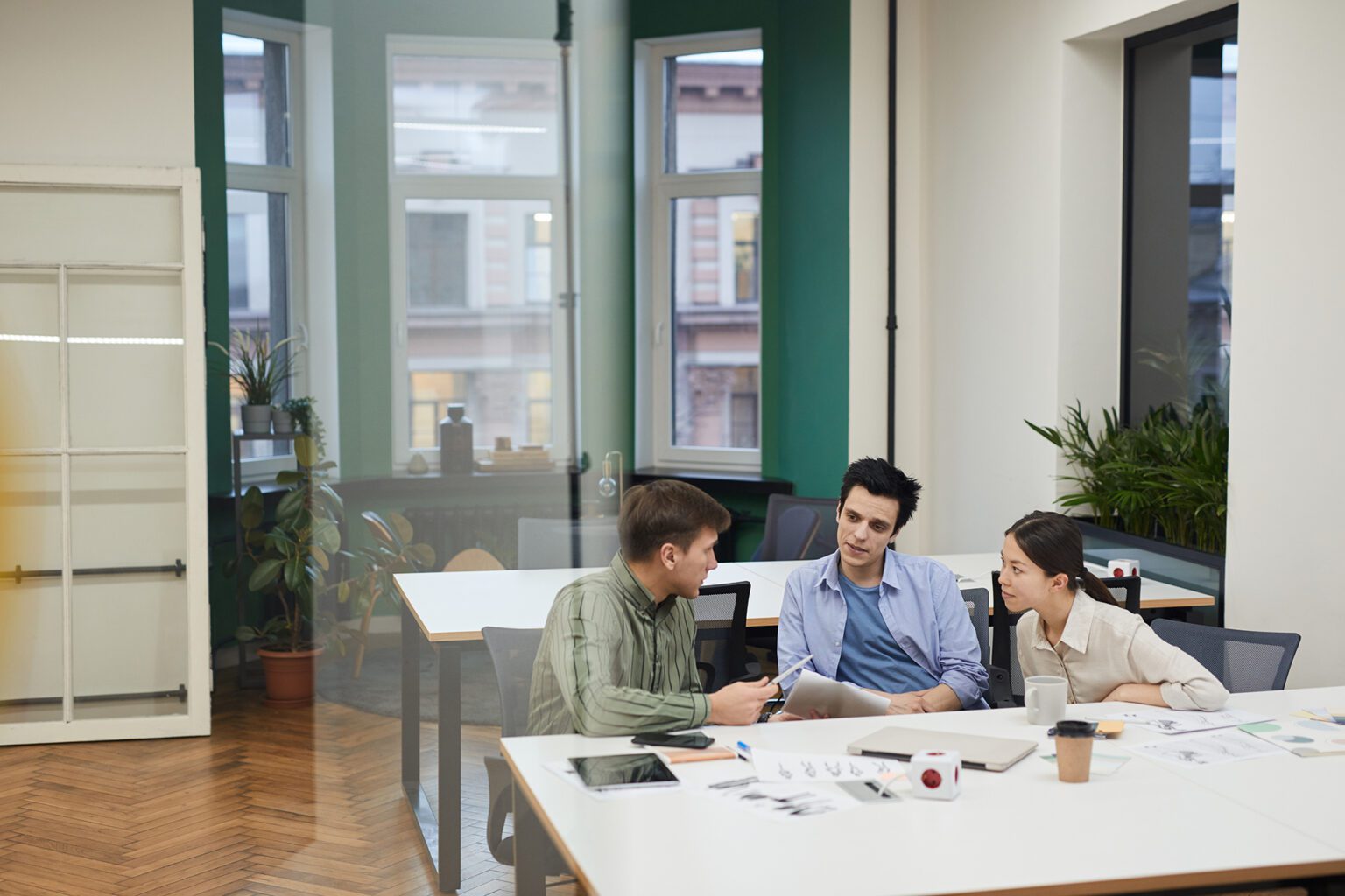 Team of designers sitting at the table and discussing new creative project together during meeting at modern office